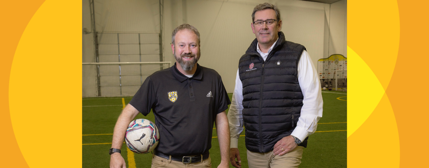 Ball Brothers Foundation President/CEO Jud Fisher (right) and 2025 Fisher Governance Award recipient Tony Pierce stand inside of an indoor soccer field. Pierce was honored for his exceptional board leadership and expanding access to youth soccer across the community.