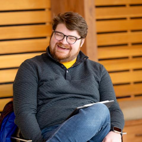 Caucasian man with brown hair and glasses, sitting down