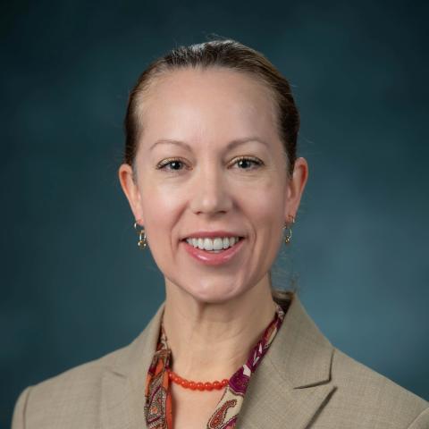 Caucasian woman with hair pulled back and tan jacket.