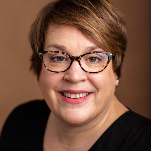 Caucasian woman with short brown hair, wearing glasses and black top