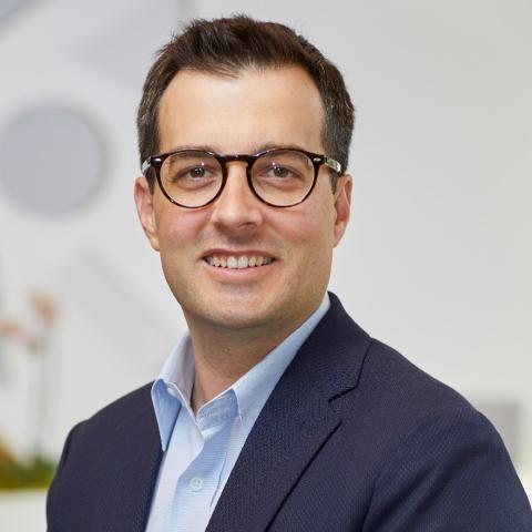 Caucasian man with dark hair and glasses and navy jacket.