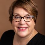 Caucasian woman with short brown hair, wearing glasses and black top